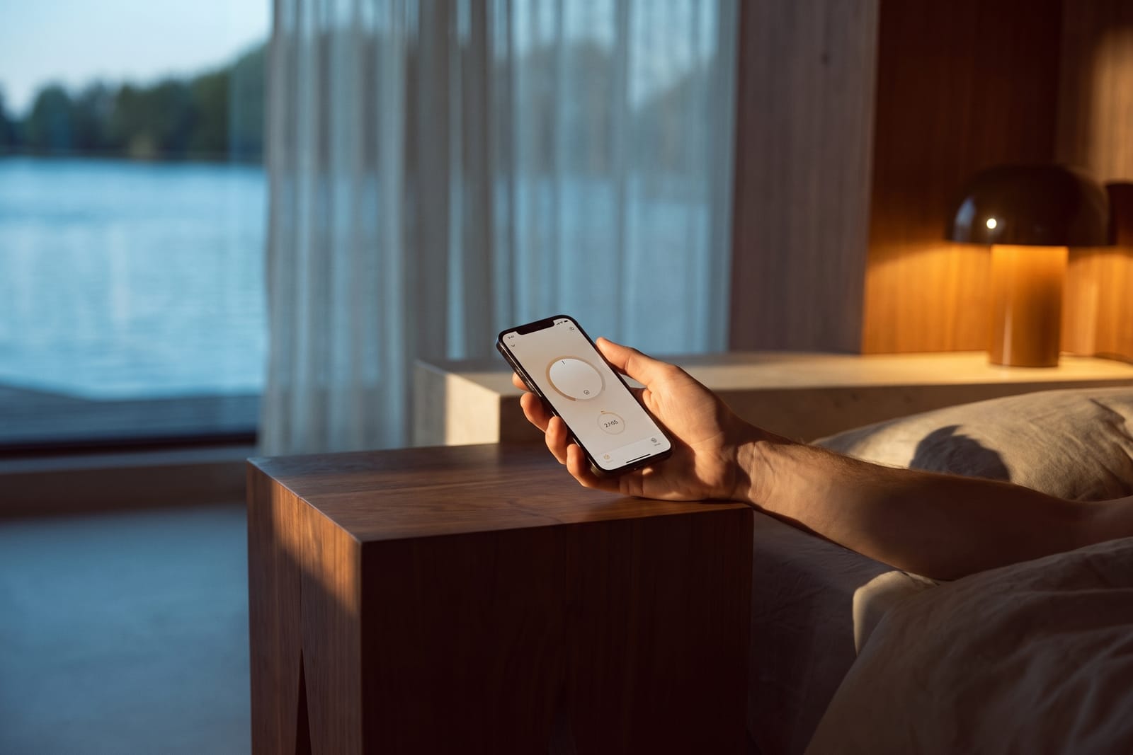 A hand reaching from the bed holds a phone with a control app